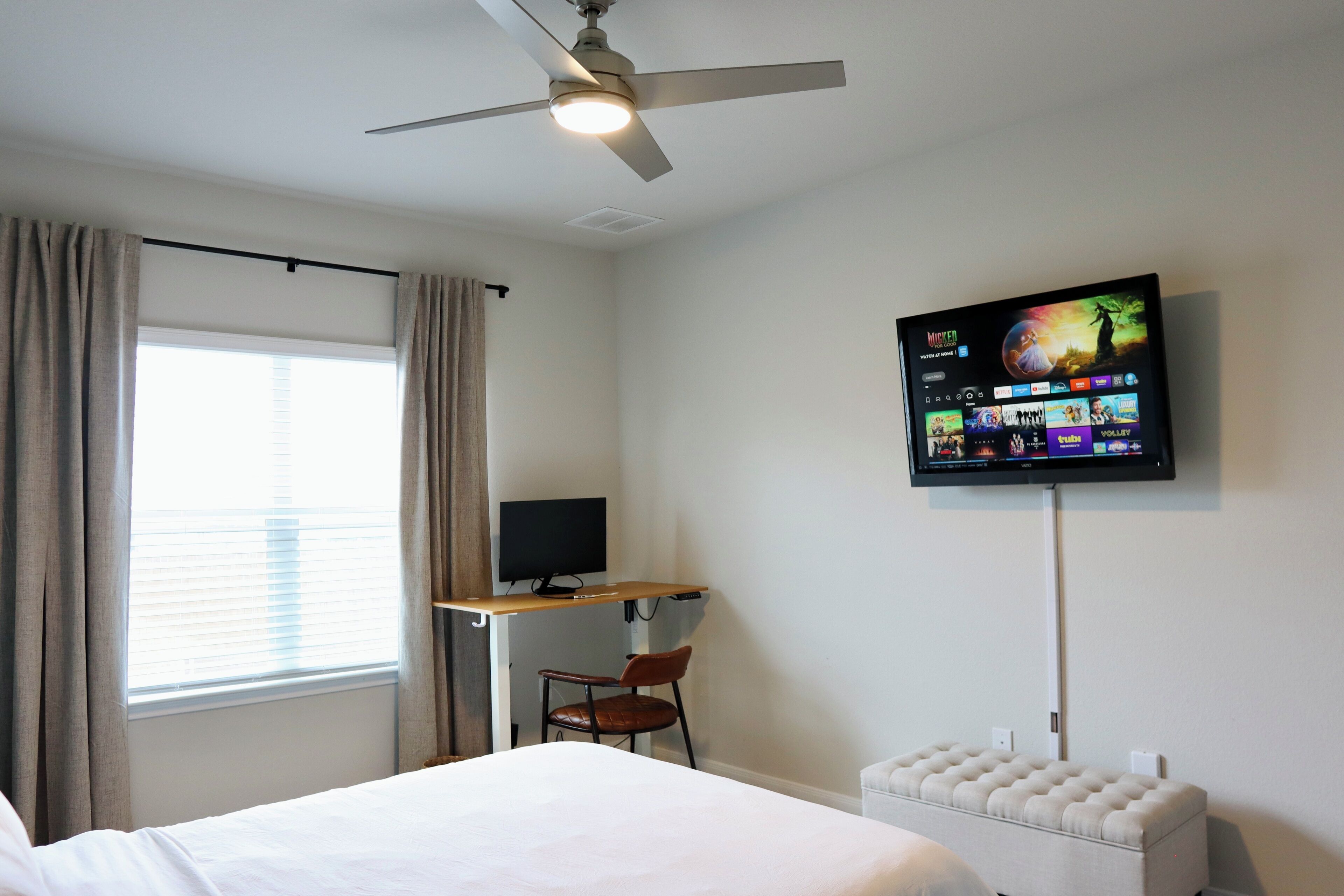 Une chambre d’hôtel équipée d’un lit, d’un bureau avec un ordinateur, d’un téléviseur fixé au mur et d’un ventilateur de plafond.