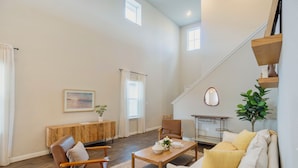 A spacious living area with a wooden coffee table, a sofa, and a chair. There is a staircase leading to an upper level. - Casa Encanto - Modern Stay, 2 Lounges, Gym & Fire Pit (Pflugerville)