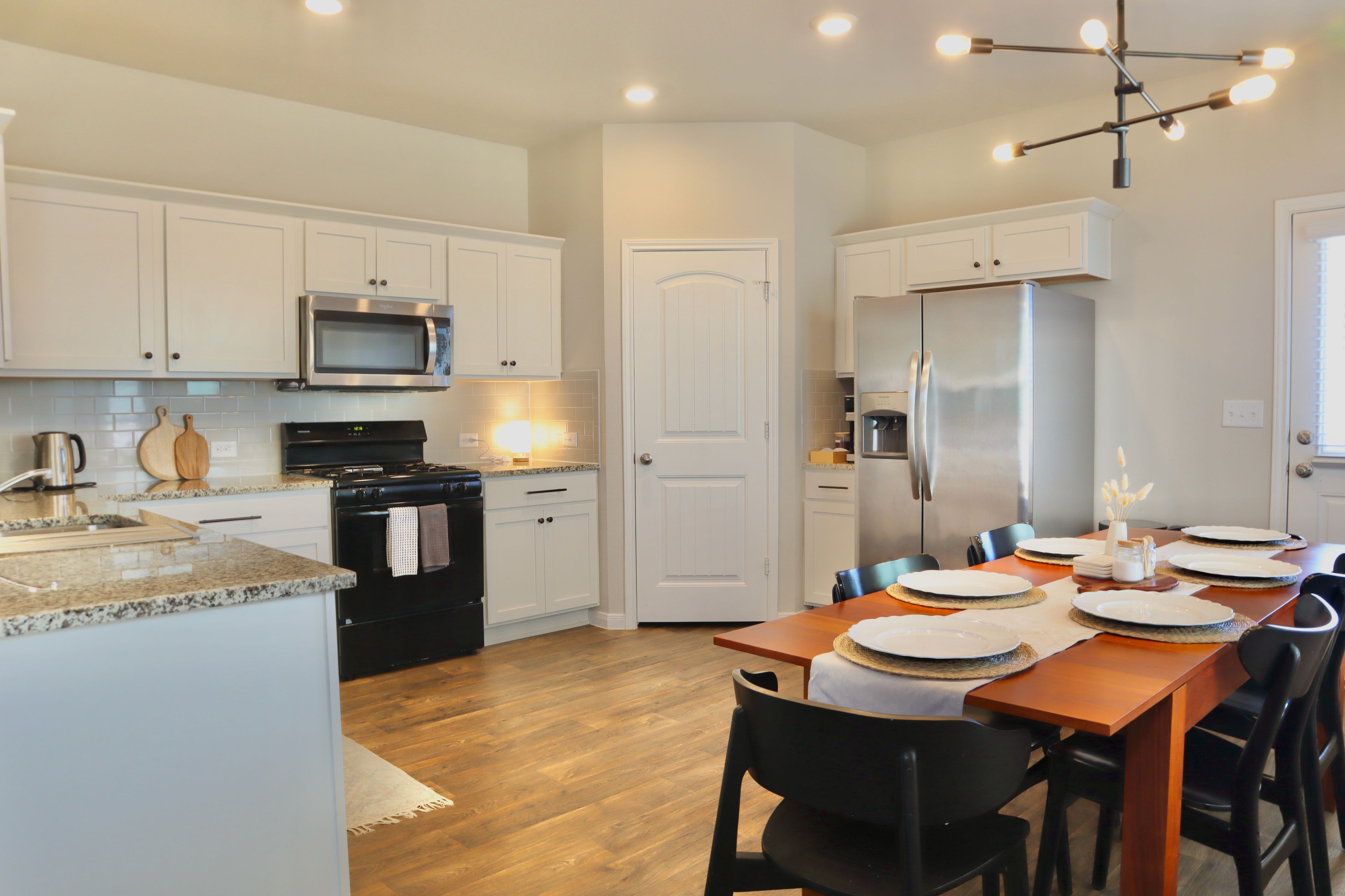 A modern kitchen with white cabinetry, stainless steel appliances, and a dining area set for six.