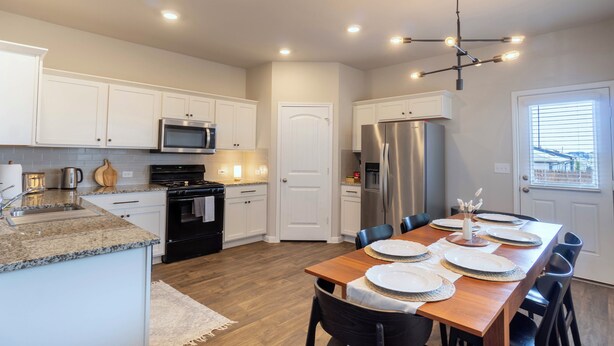 A modern kitchen with white cabinets, a stainless steel refrigerator, and a wooden dining table set for four. - Casa Encanto - Modern Stay, 2 Lounges, Gym & Fire Pit (Pflugerville)