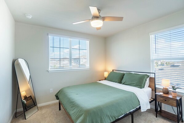 A bedroom with a bed, a nightstand, a mirror, and a ceiling fan. - Casa Encanto - Modern Stay, 2 Lounges, Gym & Fire Pit (Pflugerville)