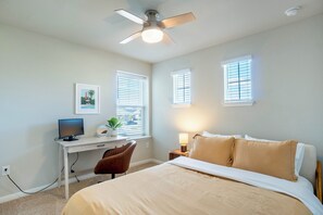 Une chambre à coucher avec un lit, un bureau avec un ordinateur, une chaise et un ventilateur de plafond.