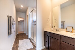 A modern bathroom with a large mirror, dark wooden cabinets, and a white countertop. - Casa Encanto - Modern Stay, 2 Lounges, Gym & Fire Pit (Pflugerville)