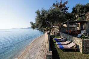 Ein Hotel direkt am Strand mit Steinmauer, Liegestühlen und Blick auf das Meer.