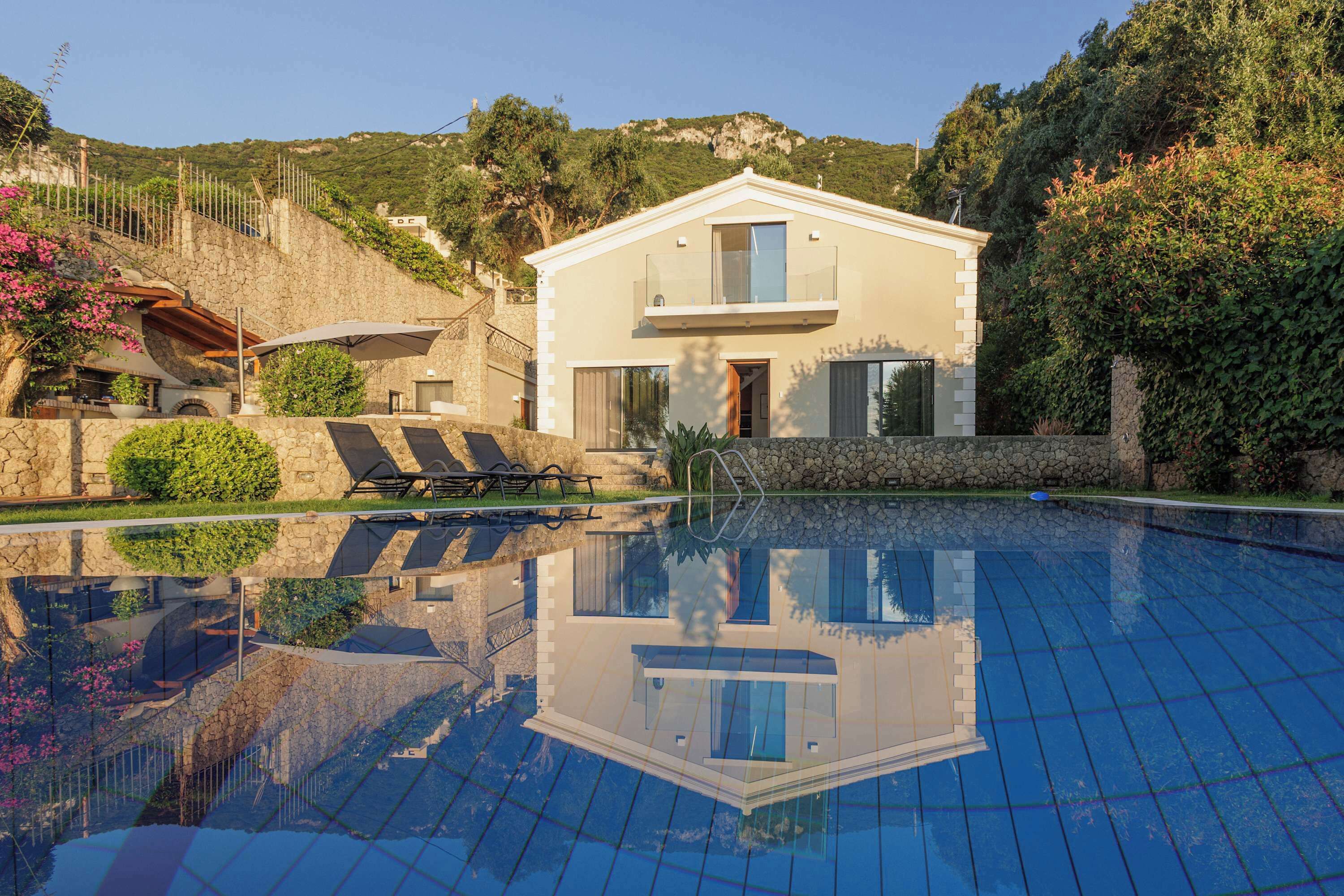 Une villa moderne dotée d’une piscine, de murs en pierre et offrant une vue sur les collines environnantes.