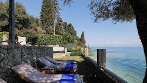 A seaside lounge area with sun loungers and a stone wall. - Villa Alia, Modern Comfort Direct Beach Access (Corfu)