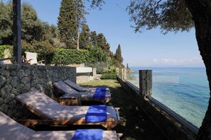 Eine Strandlounge mit Liegestühlen und einer Steinmauer.