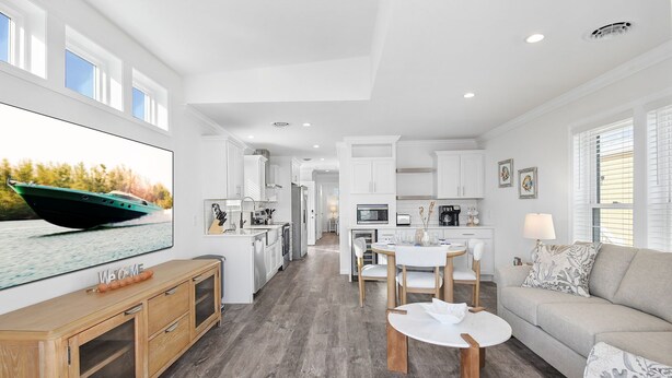 Een moderne, open woon- en eethoek met een grote televisie, houten meubels en uitzicht op de keuken.