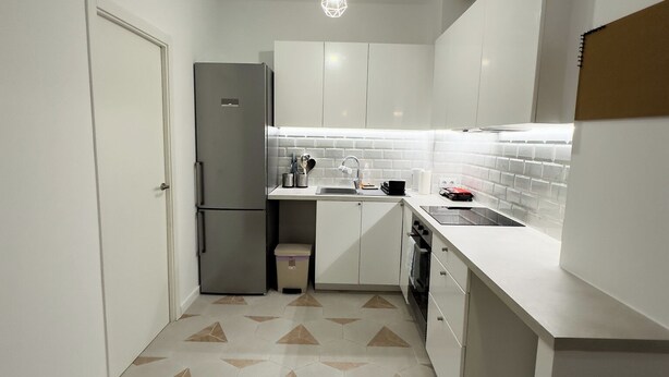 Una cocina moderna con armarios blancos, un refrigerador de acero inoxidable, un lavamanos y un piso con diseño.