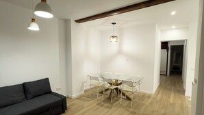 Una sala de estar moderna con un sofá negro, una mesa de comedor de vidrio y sillas, e iluminación colgante.
