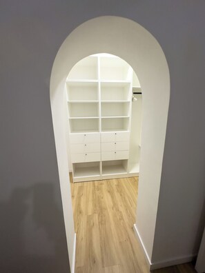 Ein begehbarer Kleiderschrank mit mehreren Regalen und Schubladen, einem Holzboden und einem weißen Durchgang.