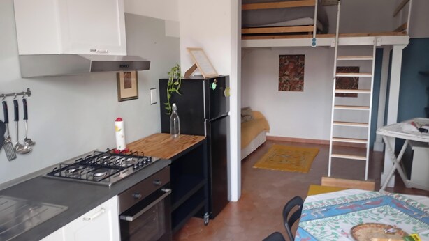 Une cuisine de taille réduite, équipée d’une cuisinière à gaz, d’un réfrigérateur noir et de meubles blancs.