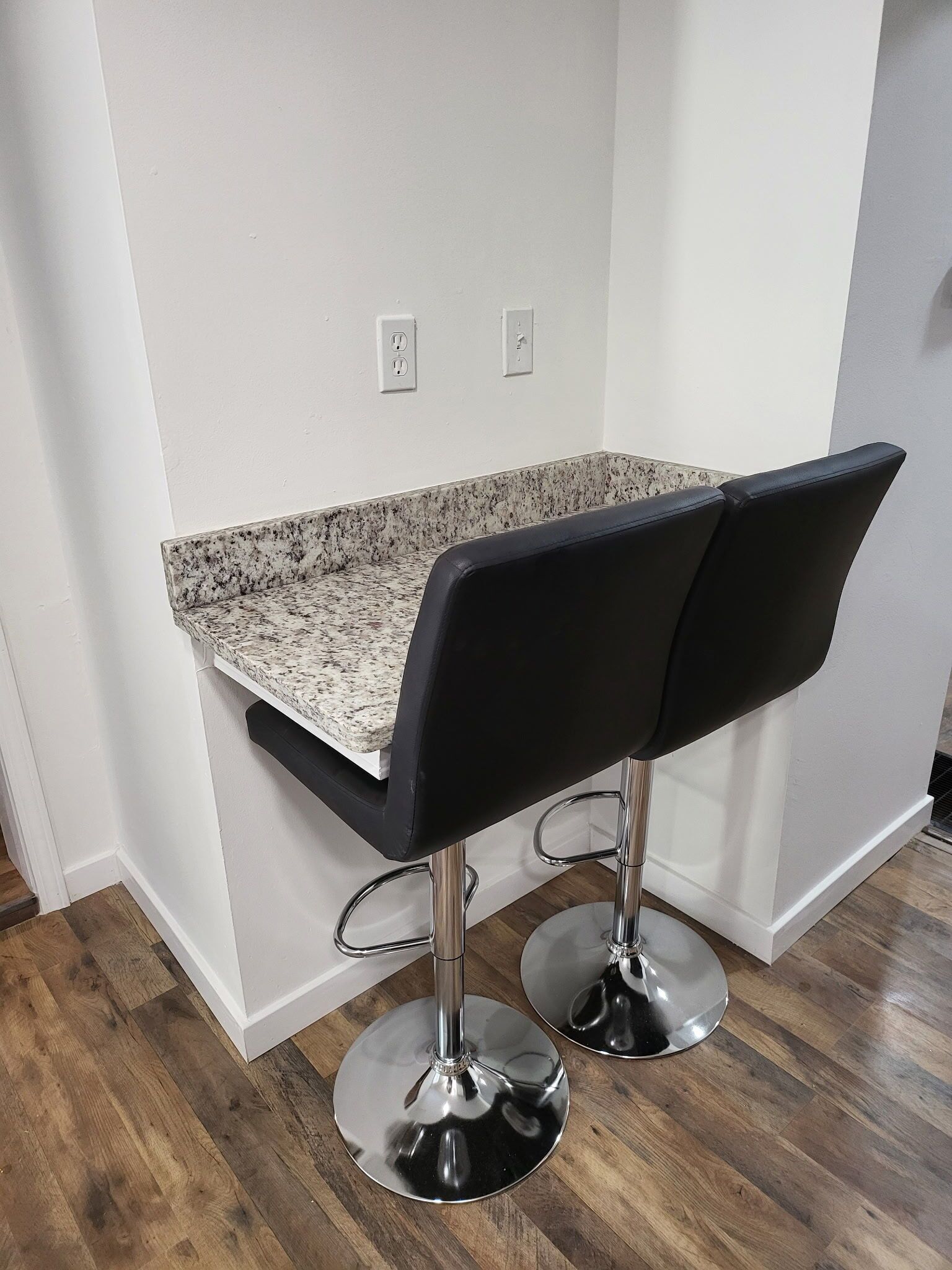 A kitchen with a granite countertop and two black bar stools with chrome bases.