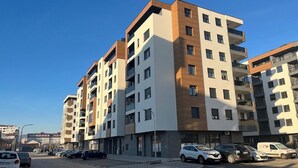 Ein mehrgeschossiges Wohnhaus mit Balkonen, einem Parkplatz und blauem Himmel.
