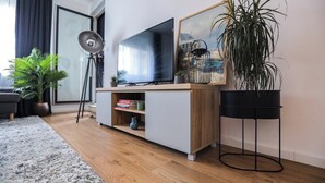 Ein modernes Wohnzimmer mit einem Flachbildfernseher auf einem Holztv-Schrank, einer Topfpflanze und einem gerahmten Bild an der Wand.