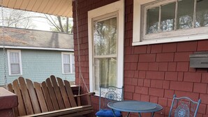 Un patio couvert comprenant deux chaises en métal bleu et une petite table ronde, un banc en bois et un ventilateur en métal.