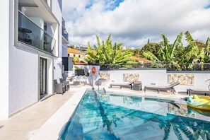 A modern pool area with a clear pool, lounge chairs, and a view of a hillside with tropical plants.