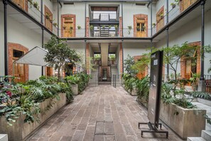 Une cour avec un sol en briques, des plantes en pot et un escalier central menant aux étages supérieurs.