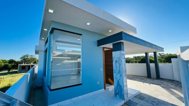 Un edificio moderno con entrada de vidrio, un espacio exterior cubierto y cielo despejado.