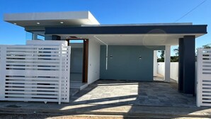 Una casa moderna con un porche cubierto, un camino de entrada empedrado de piedra y una cerca blanca.