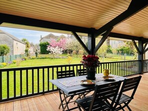 A covered patio with a table and chairs, a potted plant, and a view of a garden with a fence. - HAPPY NEEZ - REBENACQ (REBENACQ)