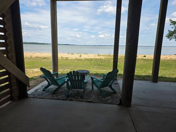 A covered patio with a view of a beach and lake.