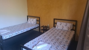 Two single beds with floral bedding, a small bedside table with a remote control, and a nightstand with a bottle. - Zennis Earth Stays (Mandrem)