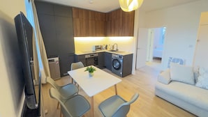 A compact living space with a kitchenette, a dining area with a table and chairs, a sofa, and a TV mounted on the wall. - Large Luxury Apartment Combo featuring 4 bedrooms, 4 bathrooms & 2 living rooms. (London)