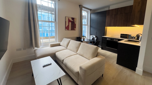 A modern living room with a sofa, a coffee table, and a kitchen area with a sink and appliances. - Large Luxury Apartment Combo featuring 4 bedrooms, 4 bathrooms & 2 living rooms. (London)