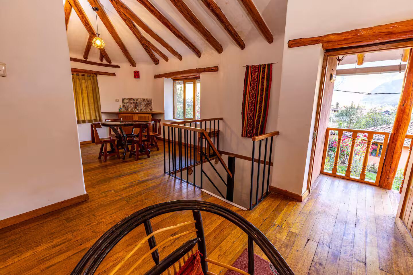 A spacious room with wooden floors, a dining area with a table and chairs, a staircase with a wooden railing, and a view of greenery outside.