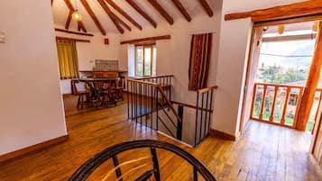 A spacious room with wooden floors, a dining area with a table and chairs, a staircase with a wooden railing, and a view of greenery outside.