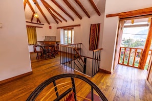 Une pièce spacieuse avec un plancher en bois, un coin repas comprenant une table et des chaises, un escalier avec une rampe en bois, et une vue sur la verdure à l’extérieur.