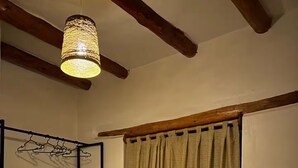 Una camera da letto con un letto, una lampada a sospensione, una testiera in legno, un comodino, una sedia e una finestra con tende.