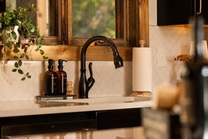 Cozinha com torneira moderna, moldura de janela de madeira e painel de azulejos brancos.