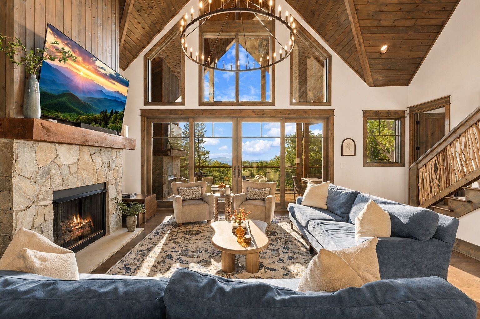 A spacious living room with a stone fireplace, a large sofa, and a television mounted on the wall.