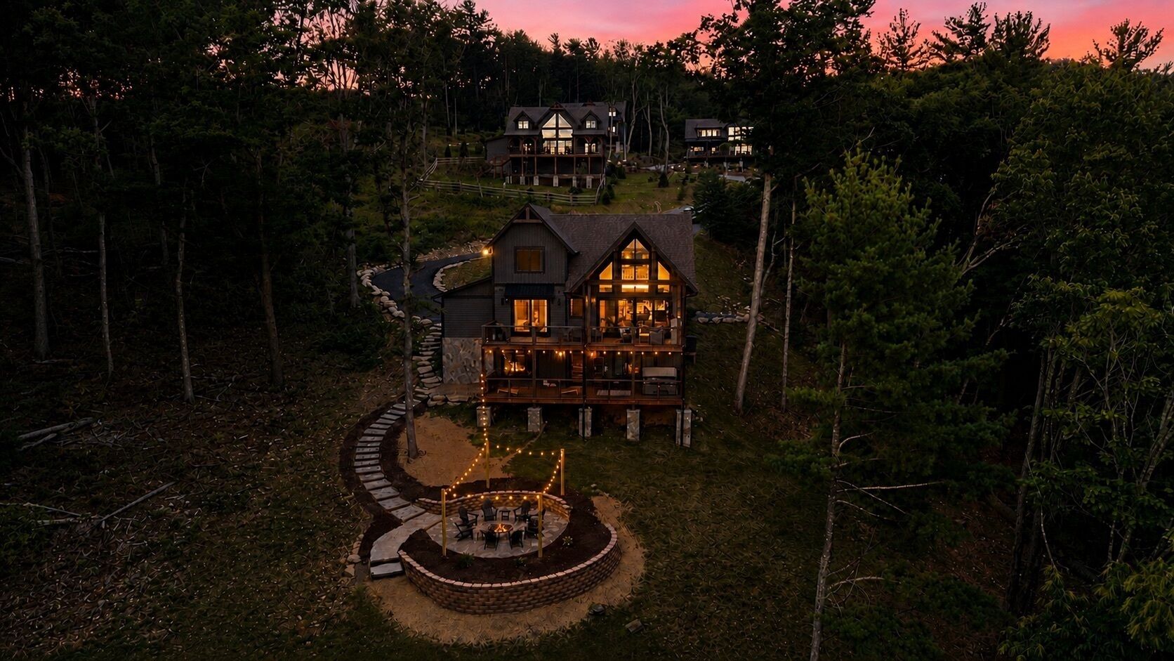 A large, multi-story lodge with a well-lit patio area, surrounded by dense forest.