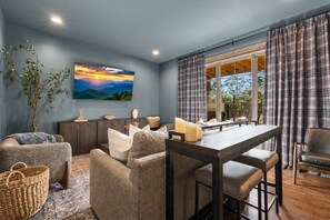 Uma sala moderna com área de jantar, uma janela grande com cortinas, um quadro na parede e uma planta.