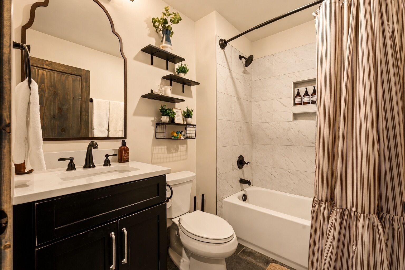A bathroom with a white sink, black cabinets, a toilet, a bathtub, and a shower curtain.