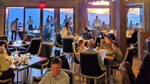 Ein Restaurant mit Tischen, Stühlen, großen Fenstern und einem Hinweisschild für den Ausgang.