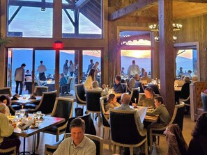 Restaurante com mesas, cadeiras, janelas amplas e placa de saída.