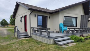 A modern building with a covered outdoor area, steps leading to a deck, and a red door.