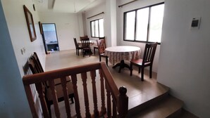 A dining area with a round table and chairs, a staircase, and a window with blinds. - Breezy 18-Room Bed and Breakfast Perfect for Family Celebrations, Conferences (Manoc-Manoc, Boracay)