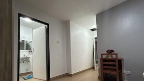 A hallway with a wooden floor, a door leading to a bathroom, and a small wooden table with a vase of flowers. - Casa de la 2-bedroom townhome in charming Lilongwe neighborhood (Lilongwe)