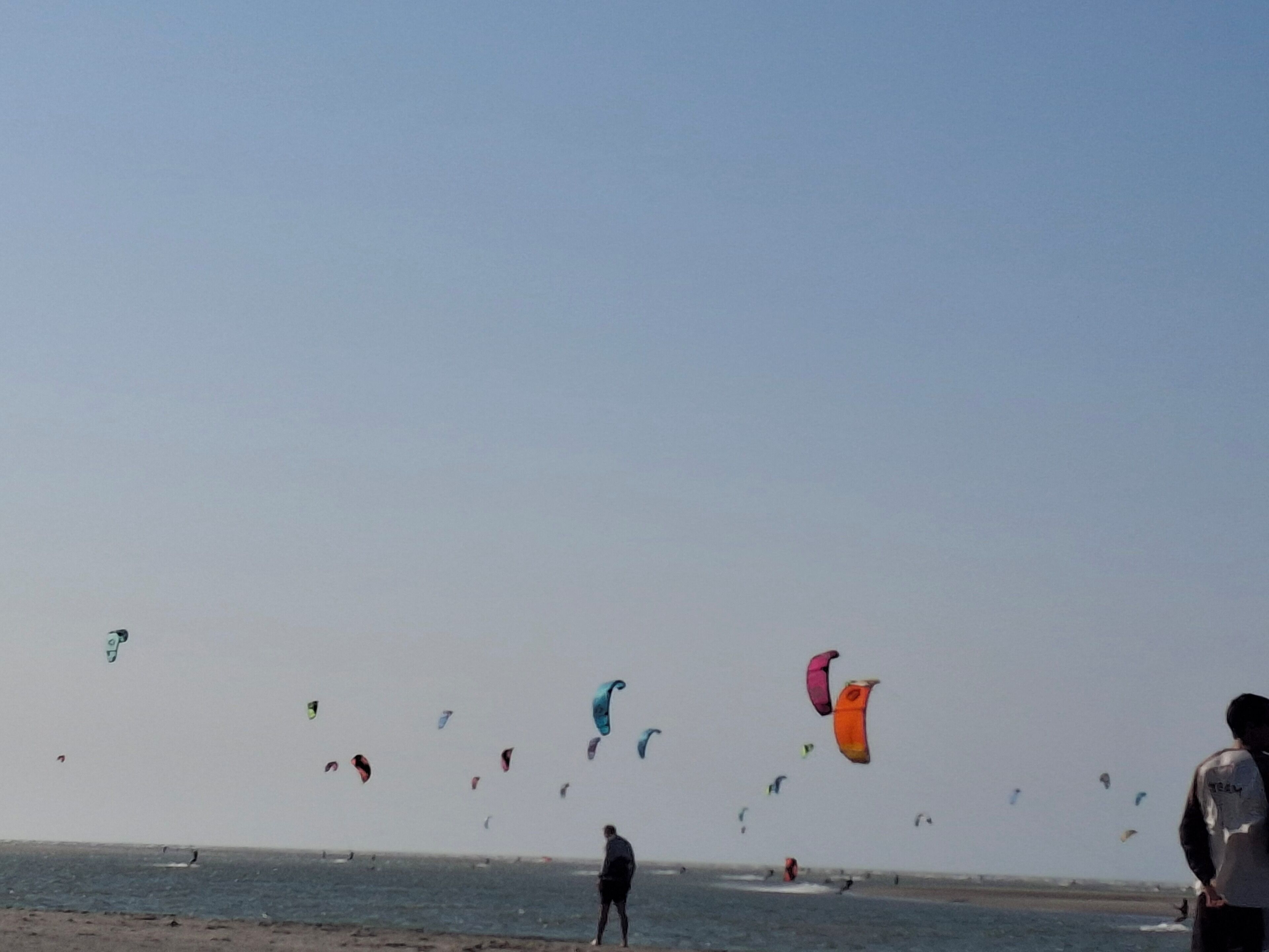 Ein Strand mit Menschen und bunten Drachen am Himmel.