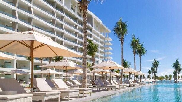 A hotel pool area with sun loungers and umbrellas, surrounded by palm trees and a multi-story building. -  4-Bedroom Penthouse Loft.  Private Rooftop Jacuzzi, Dual Terraces, Ocean Views (Q.R.)