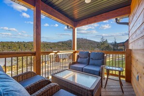 Un espace extérieur aménagé avec des meubles en osier, une table à plateau en verre et une vue sur un paysage montagneux.
