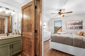 A bedroom with a bed, a ceiling fan, a window with blinds, a painting on the wall, and a staircase leading to an upper level. - Private Hot Tub at The Bobber Stop, Arcade, Community Pools Nearby & Free Attraction Tickets (Hollister)