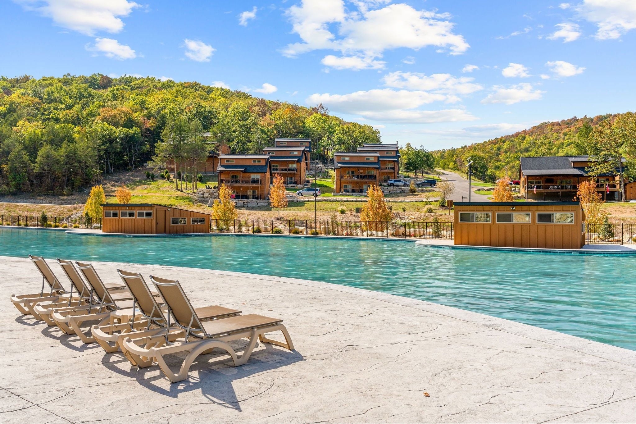 A pool area with lounge chairs and a view of a resort with multiple buildings.