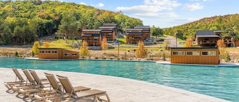 A pool area with lounge chairs and a view of a resort with multiple buildings.