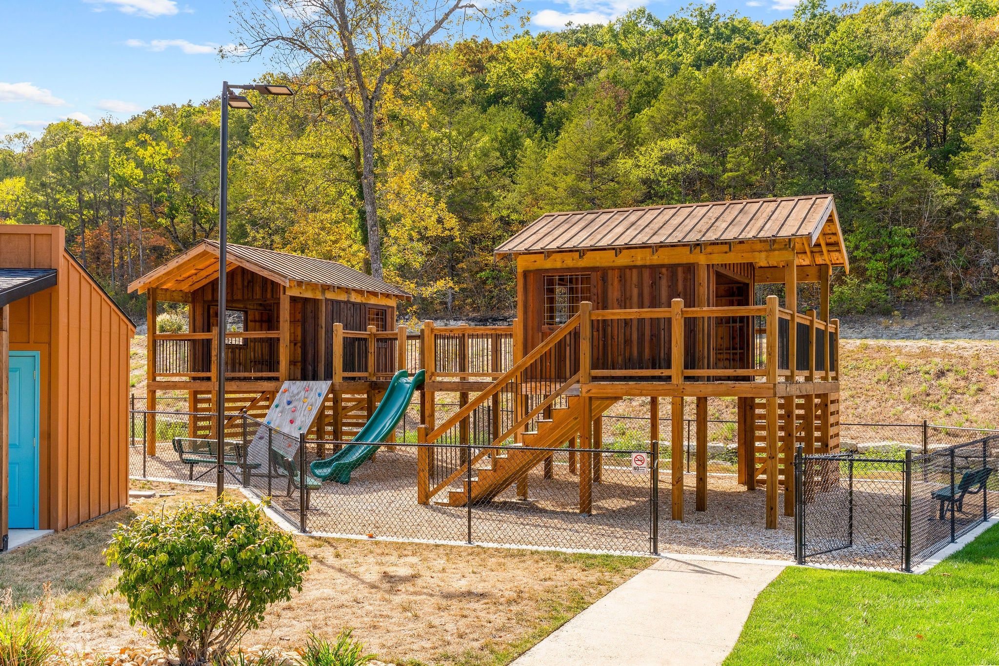A playground with wooden play structures, including a slide and climbing wall, surrounded by a fence.